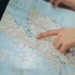 A woman's hand pointing at a location on a world map inside a car, highlighting navigation and travel planning.